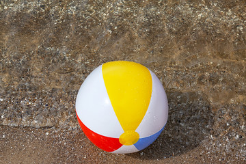 Bright inflatable beach ball on sandy beach near sea