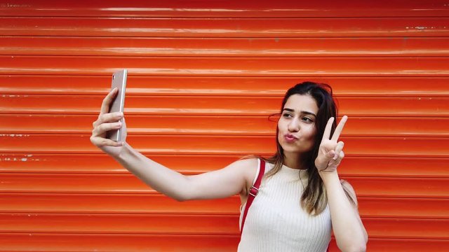 Slow motion:Beautiful young girl takes selfie with smartphone in front of orange,red background