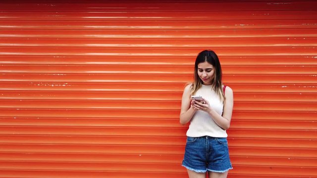 Slow motion:Beautiful young girl uses smartphone in front of orange,red background