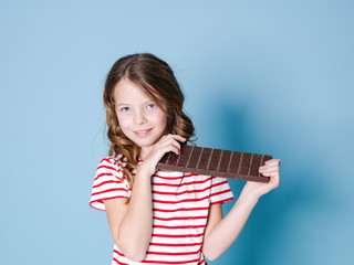 Obraz premium pretty blonde girl with a giant bar of chocolate is posing in front of blue background and is happy smiling