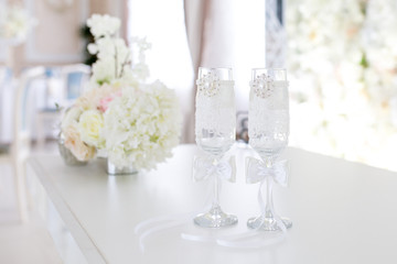Festive concept of white wedding. Flower arrangement of artificial bouquet on the table. Glasses for the bride and groom.