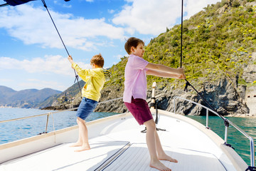 Two adorable school kid boys, best friends enjoying sailing boat trip. Family vacations on sea on sunny day. Children smiling. Brothers, schoolchilden, siblings, best friends having fun on yacht.