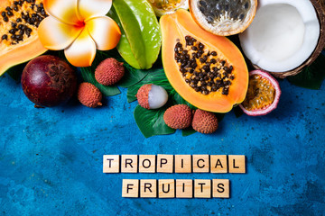 Summer tropical background with exotic various fruits, green palm leaves and flowers on blue. Fresh fruits background