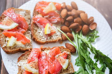 Wholemeal bread with salmon on white plate. Arugula and almond with lemon. Healthy sandwiches. Omega-3 for snack. Proper nutrition. Sport food.