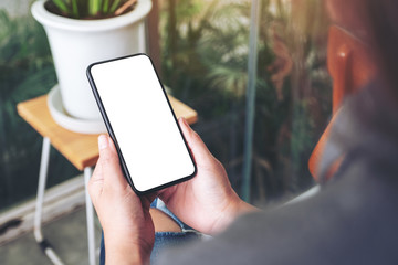 Mockup image of a woman holding and using black mobile phone with blank desktop screen in cafe