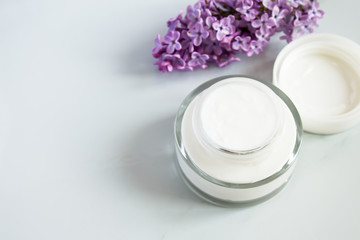 Fototapeta na wymiar Close up of facial moisturizer cream on white background. Detail of glass jar of bio moisturizer with flowers. Organic lotion for skincare treatment. Natural beauty and skin care concept.