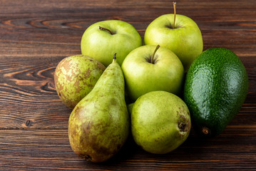 Avocado, pear and green apple on dark wooden background.