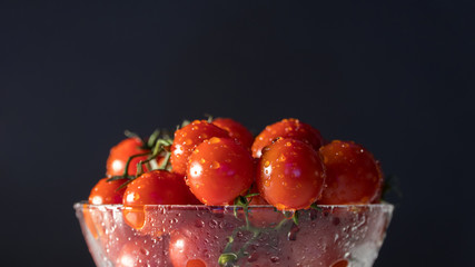 tomatoes with water drops in a glass bowl on a black background, directional lighting. horizontal plane