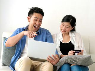Fototapeta premium Happy Asian couple shopping online with holding credit card and laptop and sitting at home together, lifestyle concept.