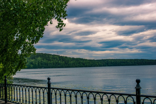 Cloudy summer sky over the calm lake and lonely tree on the front. Russian landscape.