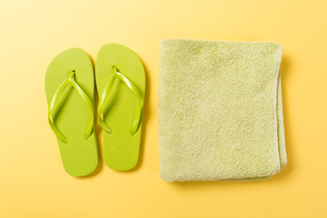Green flip flops with towel on yellow background top view flat lay with copy space. Holiday vacation travel concept with beach sea accessories
