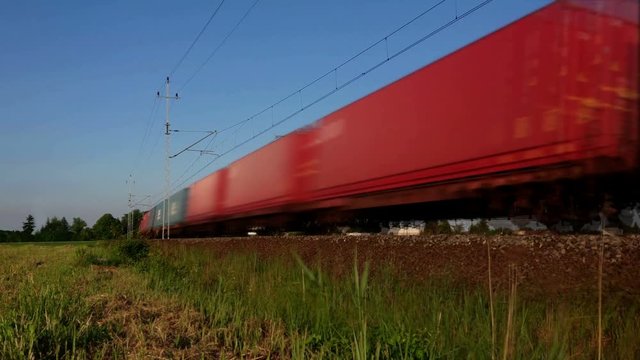A fast freight train rushes around the railroad bend – loop footage. Wagons in endless and loopable motion. Cargo transport on rail.