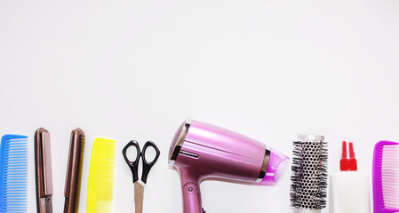 Pink hair dryer, colorful hairbrushes, comb and scissors on white background. Various hair styling devices. Top view. Hair tool set on a white table.