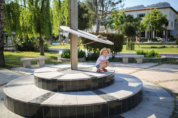child and sundial, girl plays in small square - obrazy, fototapety, plakaty