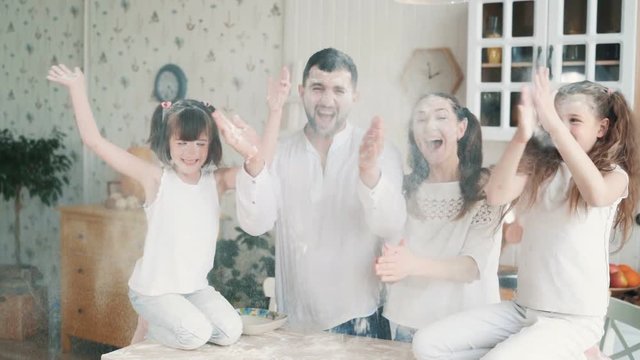 Parents and daughters soiled in flour at kitchen, laughing, playing, slow motion