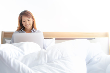 A adult woman smile  with happy face while check good news or social media in bed on laptop in the morning. A modern lifestyle of working woman or new generation to get update on internet anytime.