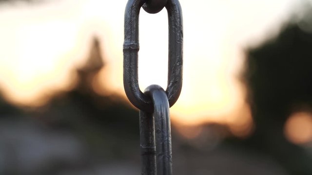 A strong, iron chain comes into focus against the backdrop of a diminishing sunset.