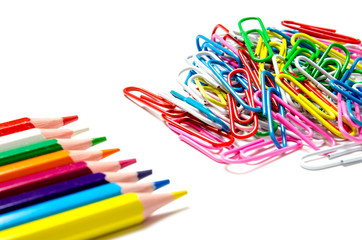Many multi-colored stationery clips for documents and multi-colored pencils lie on a white background