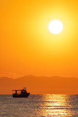 Ship at the sea in bright orange sunset / sunrise with sun in the background