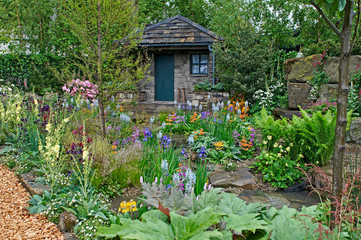 Naklejka na ściany i meble A country cottage and garden situated in a wooded rockery with a colourful display of flowers