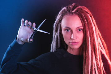 Obraz premium girl hairdresser with dreadlocks holding scissors in hand close-up