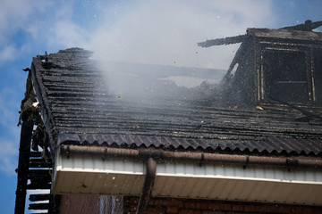 Smoldering remains of a ghetto house with a fireman spraying water