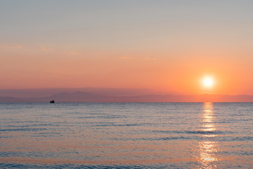 Obraz premium Ship at the sea in bright orange sunset / sunrise with sun in the background