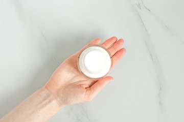Woman hand with white  hand cream on white background. Cosmetic cream container.Skin care mockup.White jar with open lid of cosmetic cream.