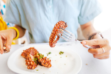 Happy asian woman in hat eating delicious grilled octopus in seafood restaurant. Delicacy and healthy gourmet cuisine