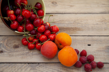 scattered berries from a plate of raspberry cherries apricots on a wooden table