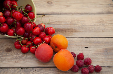 scattered berries from a plate of raspberry cherries apricots on a wooden table