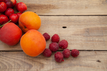 scattered berries from a plate of raspberry cherries apricots on a wooden table