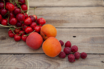 scattered berries from a plate of raspberry cherries apricots on a wooden table