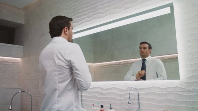 Business man setting tie in luxury bathroom. Happy man wearing necktie in house.