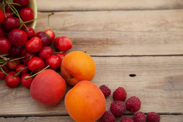 scattered berries from a plate of raspberry cherries apricots on a wooden table