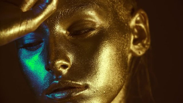 Fashion model woman golden skin face in bright sparkles, Trendy glowing gold skin make-up. Glitter metallic shine makeup