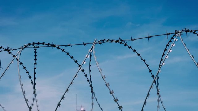 The fence of the correctional facility with barbed wire on the background of a gloomy cloudy dark blue sky.