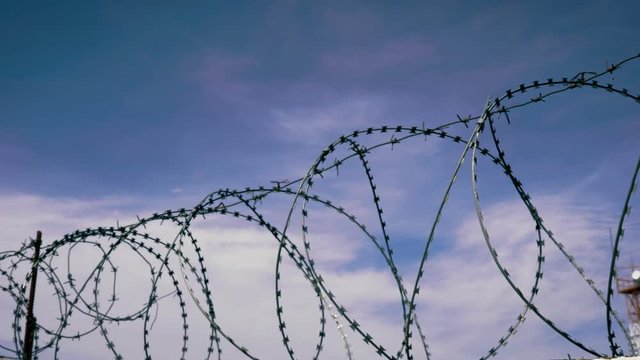 The fence of the correctional facility with barbed wire on the background of a gloomy cloudy dark blue sky.