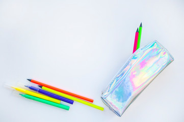 Colorful paper, neon pencils and holographic pencil case on beige background with copyspace. Flat lay style. Back to school concept.