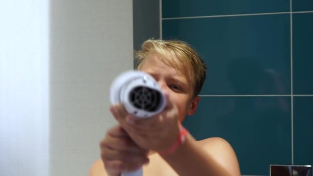 Closeup view portrait of happy cheerful playful white kid shooting with hairdryer into camera like with gun. Creativity and imagination of children concept.