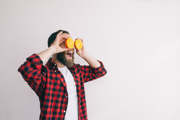 Portrait handsome young bearded man holding slices of orange in front of his eyes.
