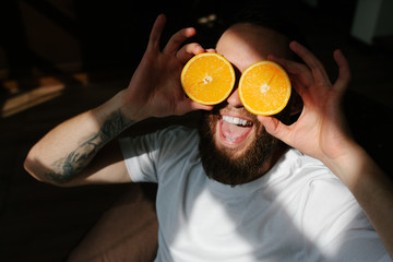 Portrait handsome young bearded man holding slices of orange in front of his eyes.
