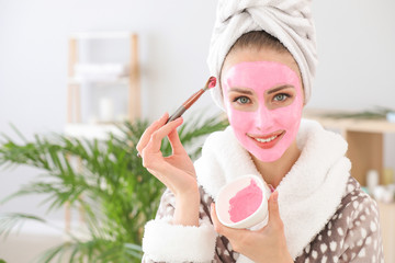 Beautiful young woman applying facial mask at home