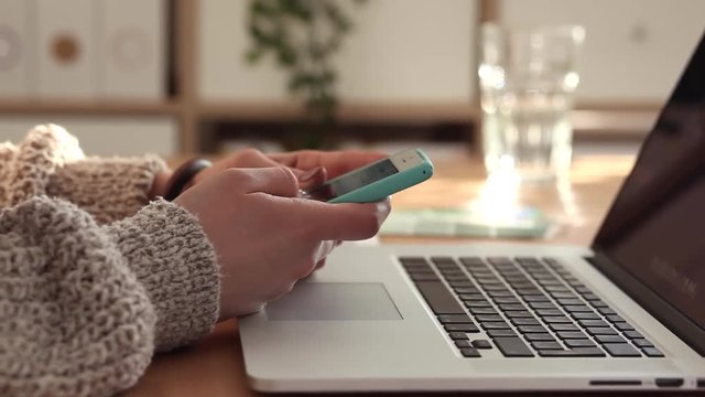 Young woman scrolls the social media feed, and writes a message using her smartphone. She's in her home office