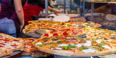 Fototapete Pizzeria Assortment of italian pizzas in a shop display. Female workers serving the pizzas.  © Rawf8