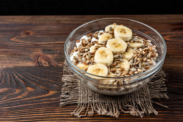 Oatmeal with cottage cheese, sunflower seeds and banana on dark wooden background with yellow tulips.