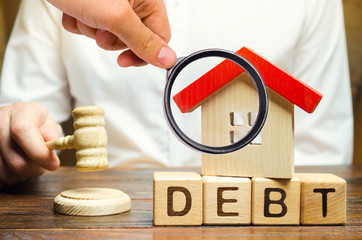 Wooden blocks with the word Debt and a miniature house with a judge's hammer. Confiscation of property for failure to pay the debt. The withdrawal of housing. Moratorium. Criminal penalty