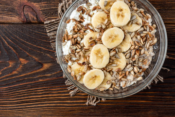Oatmeal with cottage cheese, sunflower seeds and banana on dark wooden background with yellow tulips.