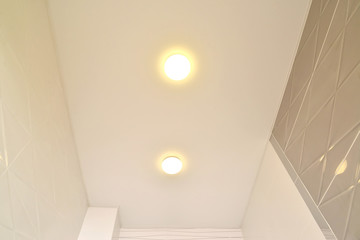Fragment of an opaque stretch ceiling with lamps in an apartment corridor