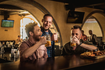 Friends drinking draft beer and watching tv in a pub